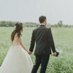 Couple holding hands in a serene field, perfect wedding photoshoot moment.